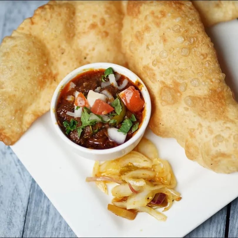 Clay Oven's chole bhature, featuring two golden fried bhature with a bowl of chana masala and pickled onions.