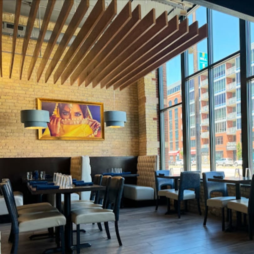 The Clay Oven dining room features modern decor, brick walls, large windows, and Indian artwork.