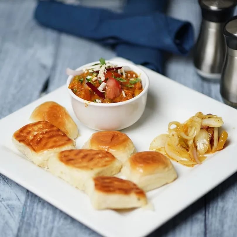 Indian pav bhaji, a vegetable curry, served with buttered pav buns and sautéed onions.