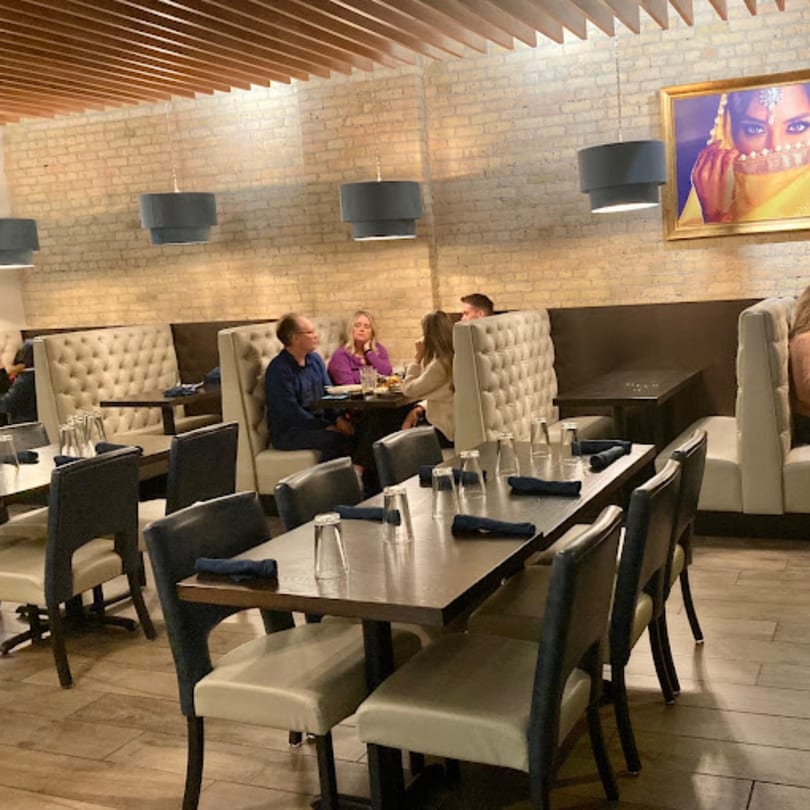 Clay Oven restaurant interior with patrons dining at tables and booths, featuring a brick wall and Indian art.