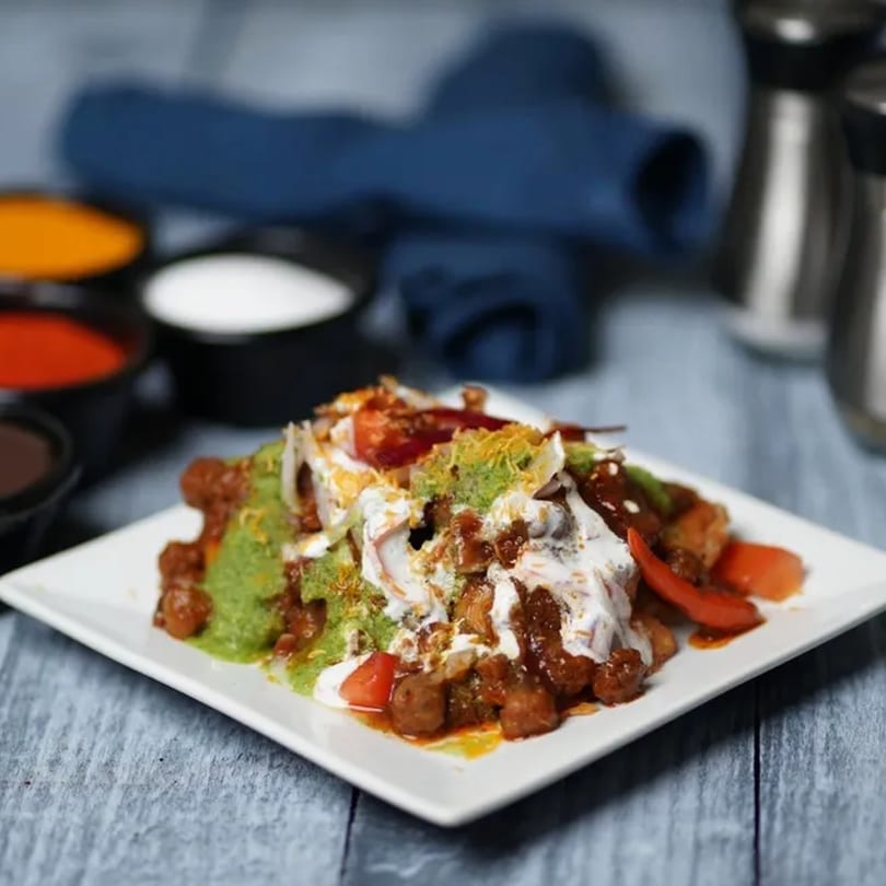 A vibrant Indian chaat dish with green chutney, yogurt, and spices on a white plate.